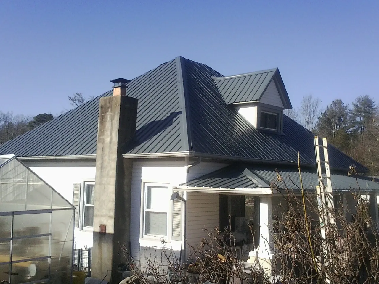 Dark blue standing seam metal roof on a white farmhouse with dormer — Slate & Tile Roof Repair by Roofing Brothers in Elmwood