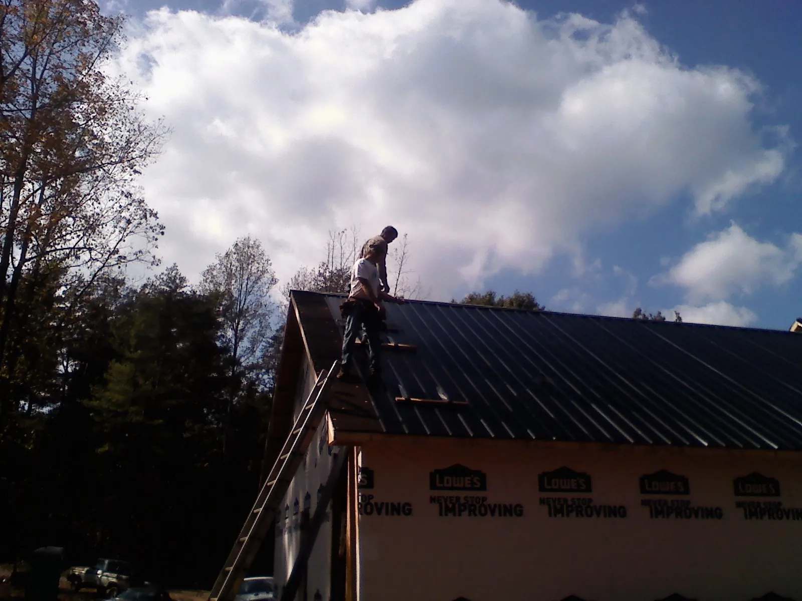 Roofer fastening dark metal panels high against a cloudy sky, from a Roof Inspection job in Elmwood