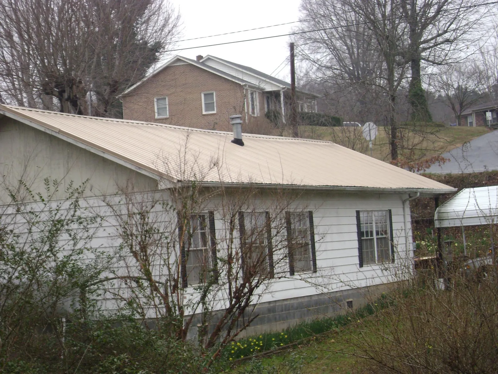 Tan metal roof on a white sided house set into a hillside — Commercial Roofing by Roofing Brothers in Elmwood