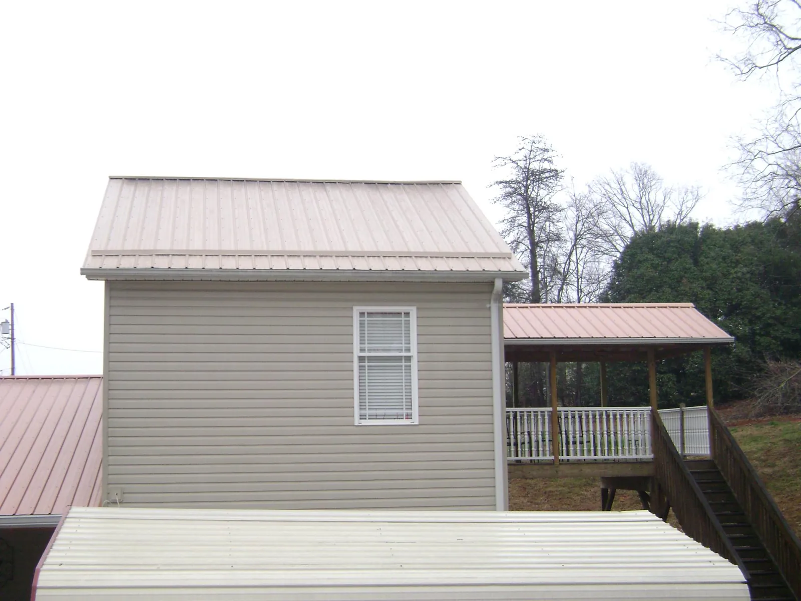Tan metal roofs on a two story addition and attached porch, from a Roof Replacement job in Elmwood